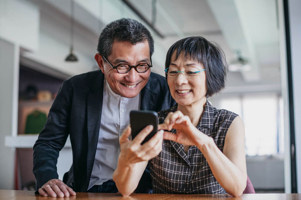 Happy asian couple checking investment on mobile phone