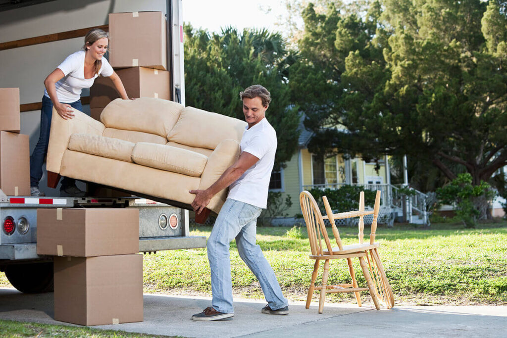 Young couple carrying couch out of removals truck into their new home